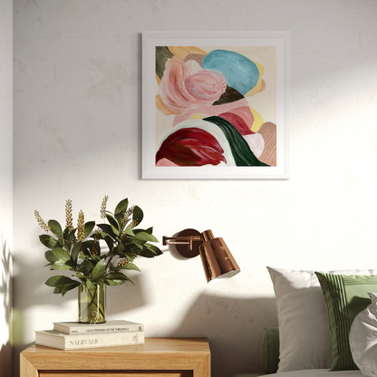 There is so much to tell, Abstract Fine Art Print on Paper with a classic frame of sustainable sourced wood in a white finish. This artwork has nature inspired abstract shapes with playful movements. Green, white, orange, yellow, pink, wine-red, sand, blue. Hanging on a white wall in a modern bedrooom next to the bed. There are green and white cushions, green plant on the side table in wood and a copper wall lamp.  Ingeborg Andersson Art